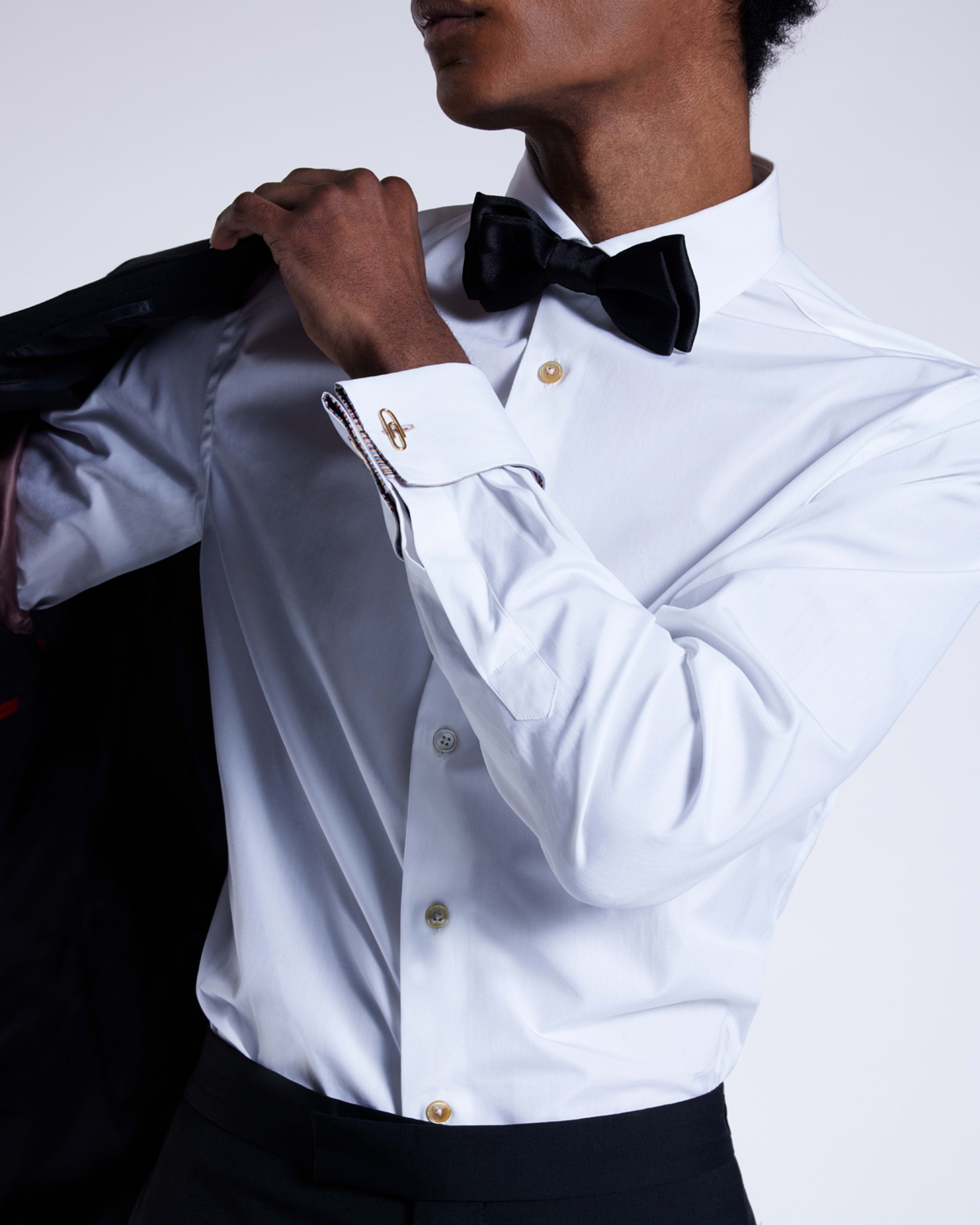 a male model putting a black tuxedo jacket on over a white shirt with black bow tie