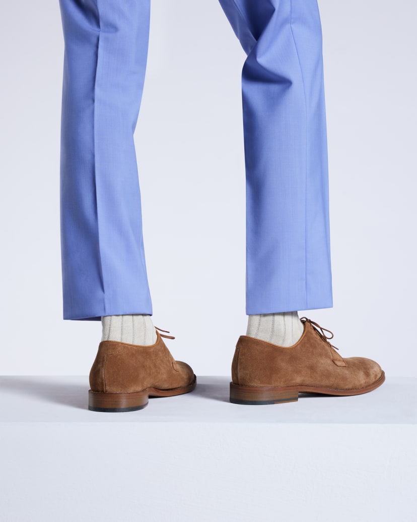 a male models legs wearing light blue suit trousers, paired with cream socks and brown suede derby shoes