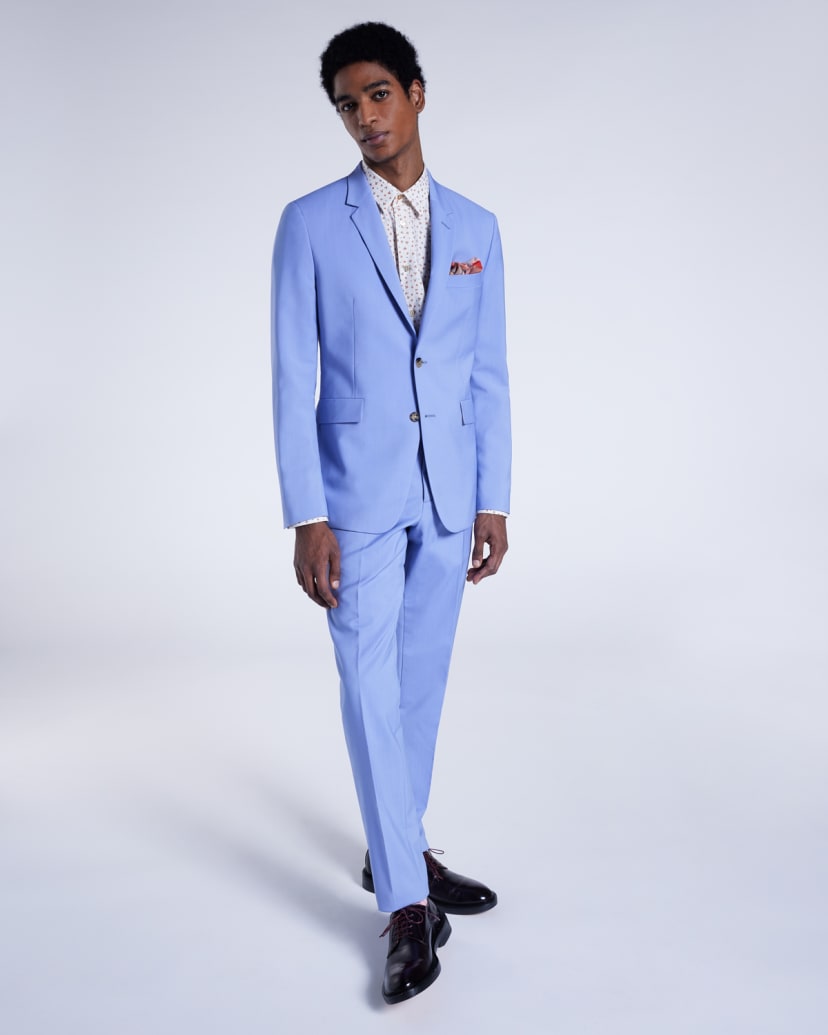 a male model wearing a light blue wedding suit with a white and red spotted shirt, red pocket square and black leather derby shoes