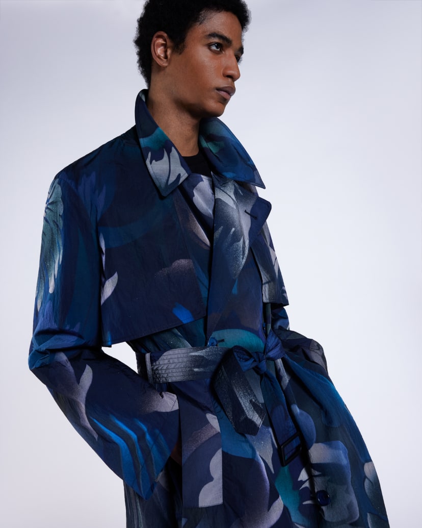 a male model wearing a blue and green patterned statement long coat with his hands in the coat pockets