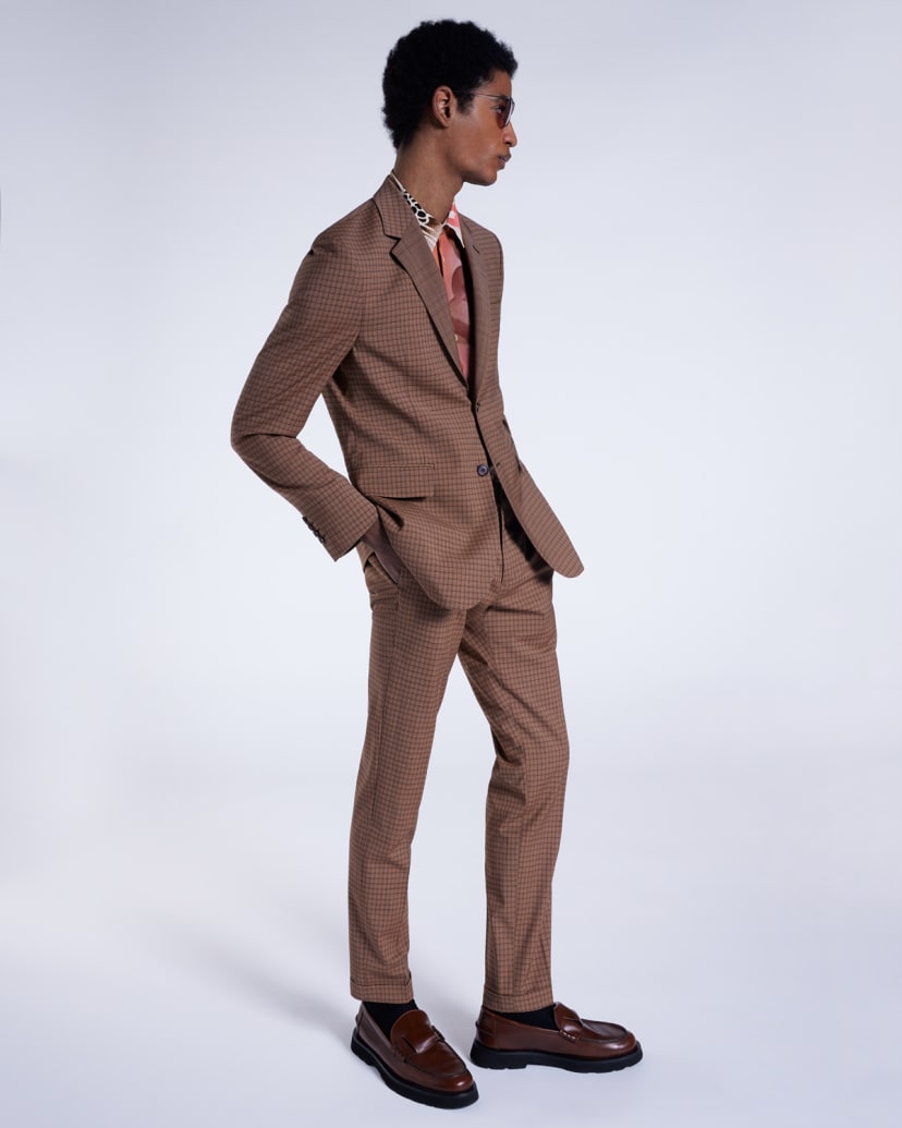 a male model wearing a designer brown checked suit with a patterned statement shirt and dark brown loafers