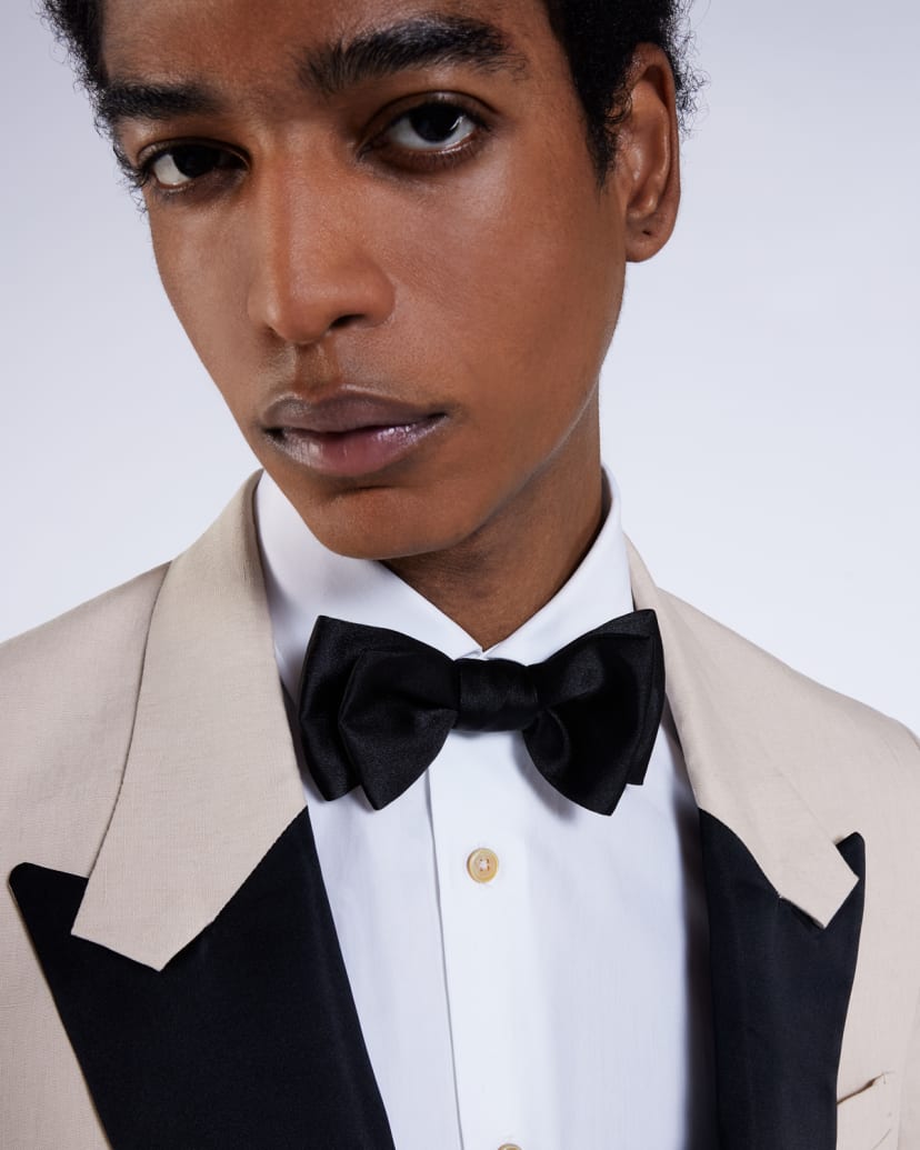 a male model wearing a beige and black tuxedo suit jacket, with black bow tie and white shirt